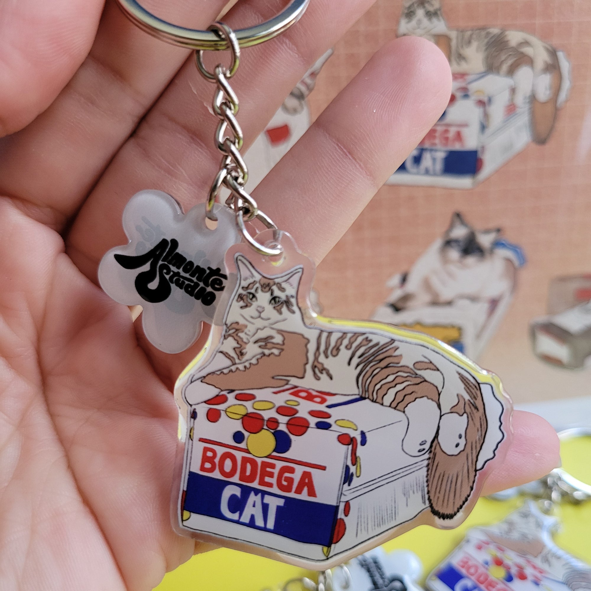 Keychain with a bodega cat design held by a hand against a colorful background.