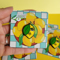 Hand holding a card with a lemon girl pin against a yellow background