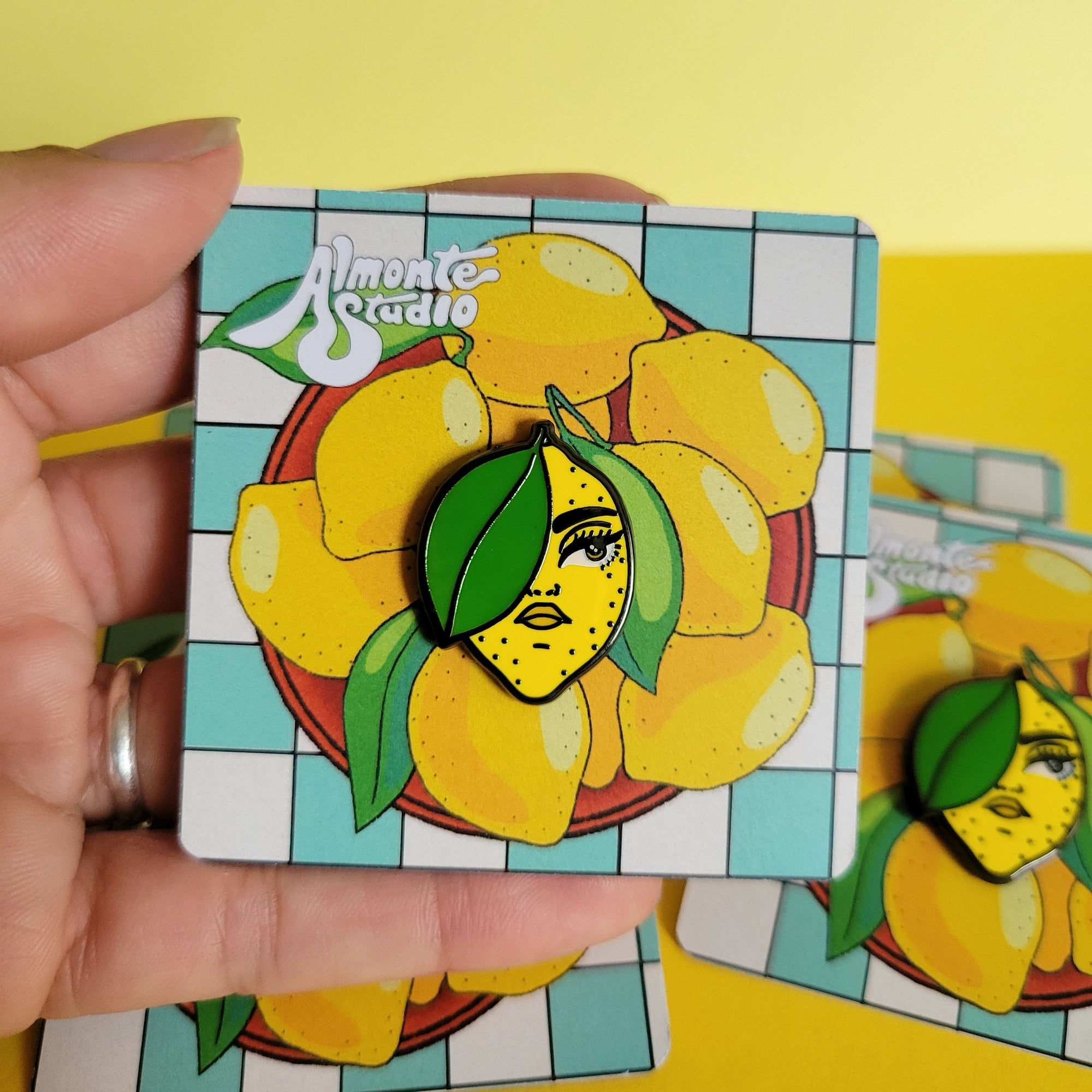 Hand holding a card with a lemon girl pin against a yellow background