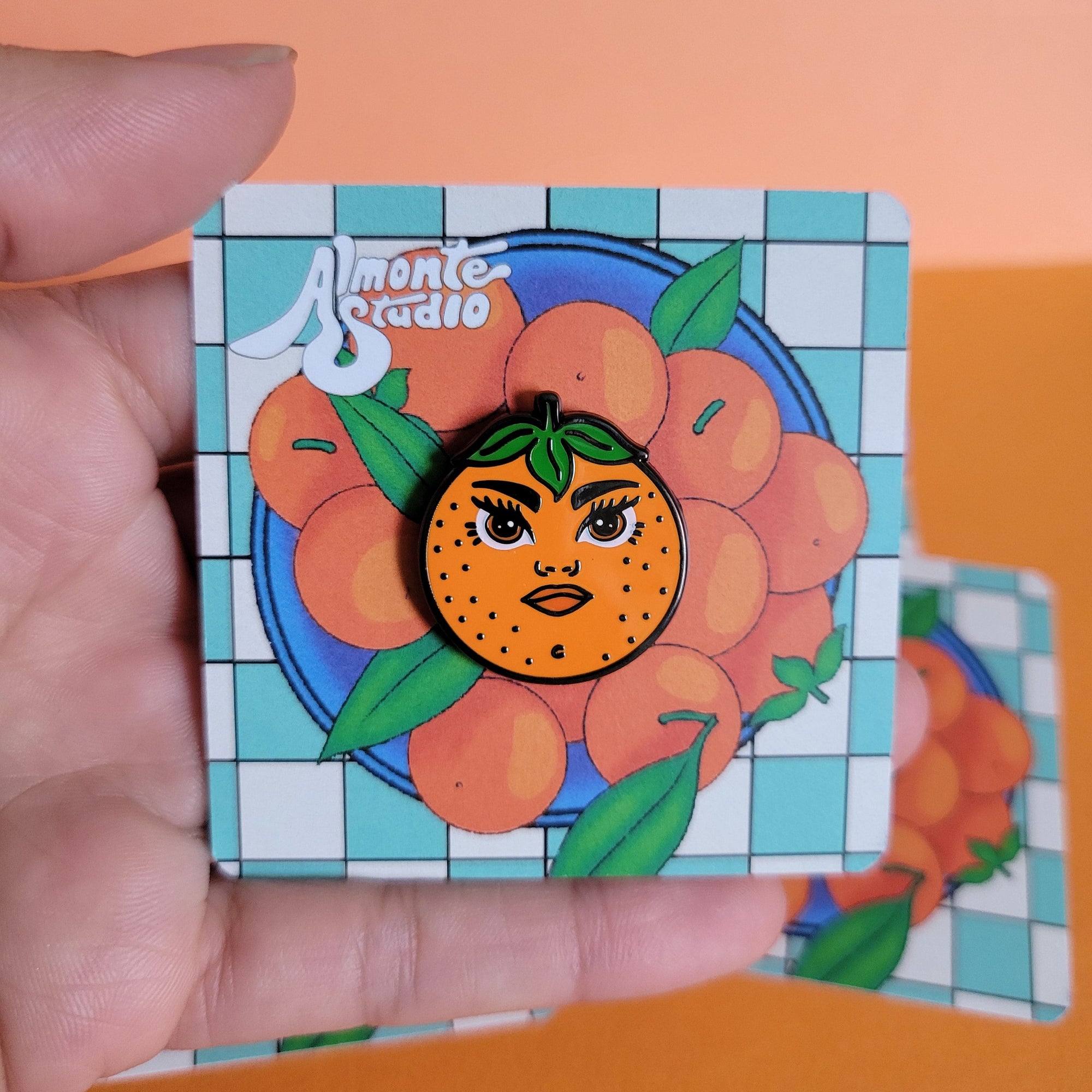 Hand holding a card with a pin of an orange with a face on a colorful background