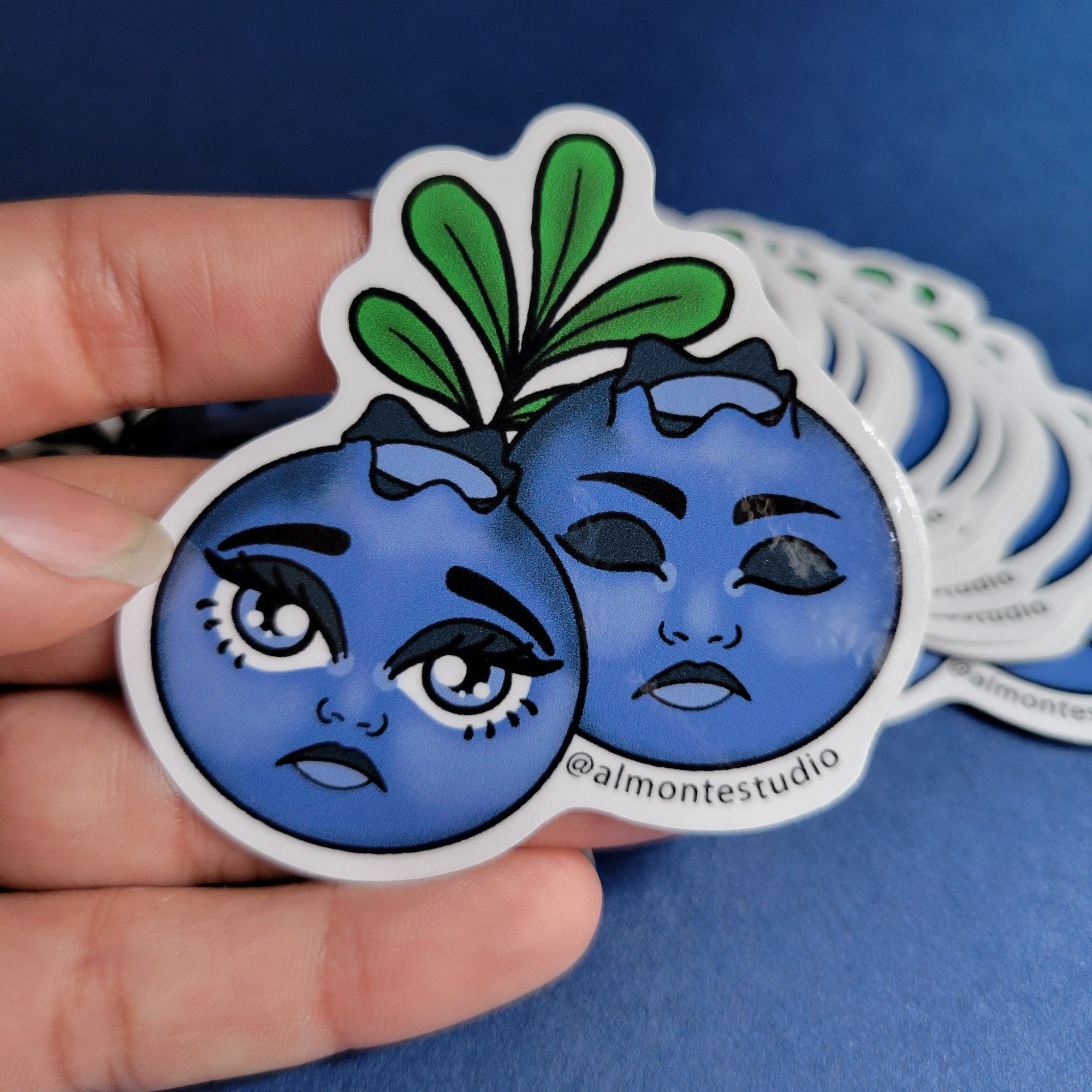Hand holding a blue and green decorative sticker with artistic design on a blue background