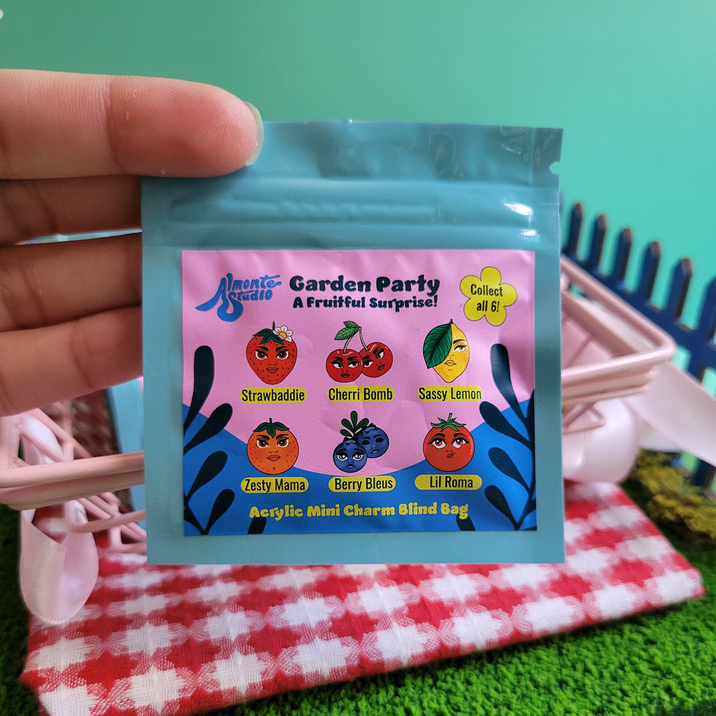 Hand holding a small colorful blind bag package with graphics on a green surface